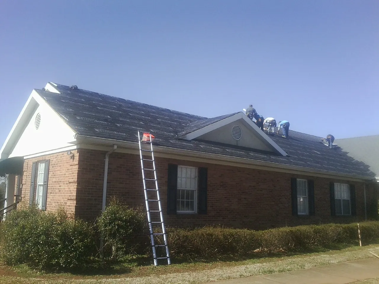 Crew tearing shingles off a brick ranch roof with a ladder set — Metal Roof Repair work by our crew in Kingsland