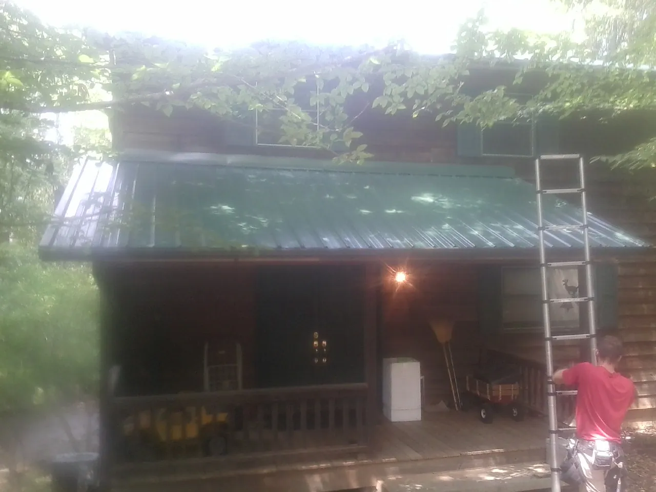 Worker on a ladder at the green porch roof of a wooded cabin in Kingsland
