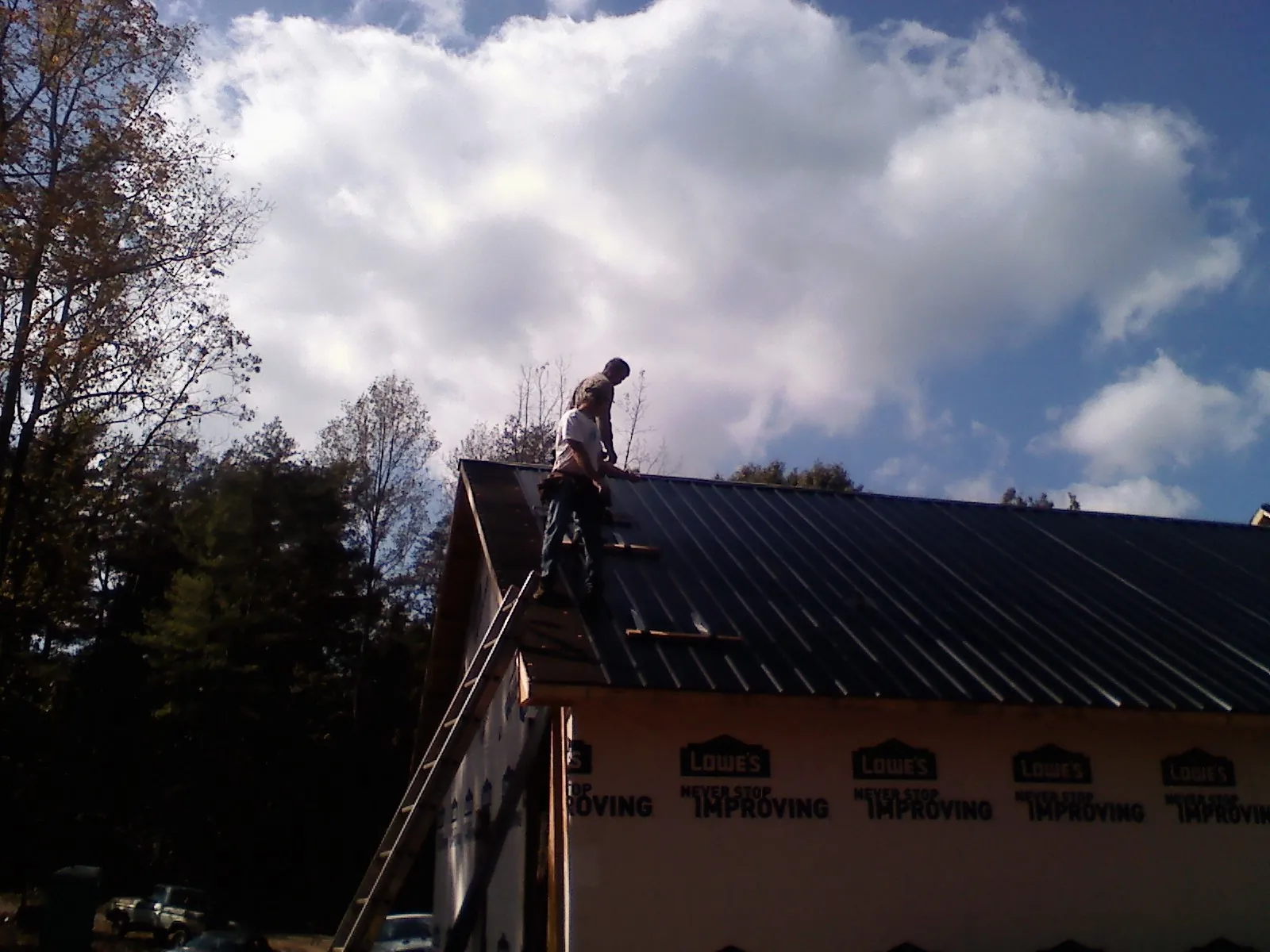 Roofer fastening dark metal panels high against a cloudy sky, from a Roof Inspection job in Kingsland