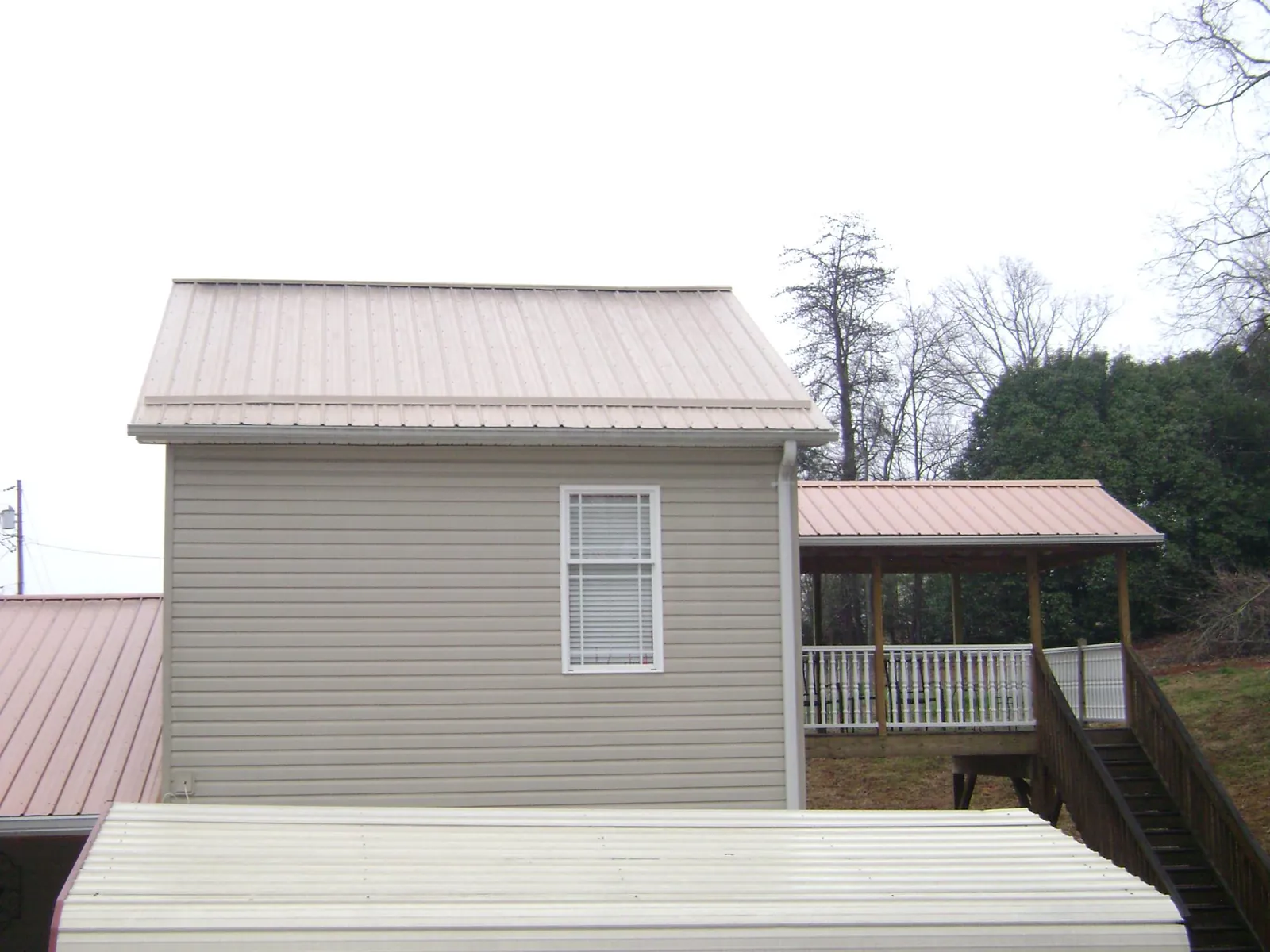 Tan metal roofs on a two story addition and attached porch, from a Roof Replacement job in Kingsland